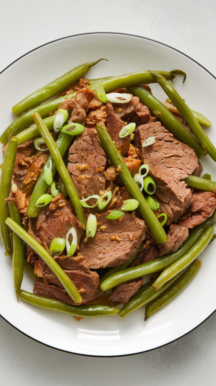 A plate of garlic beef with green beans topped with sliced green onions.